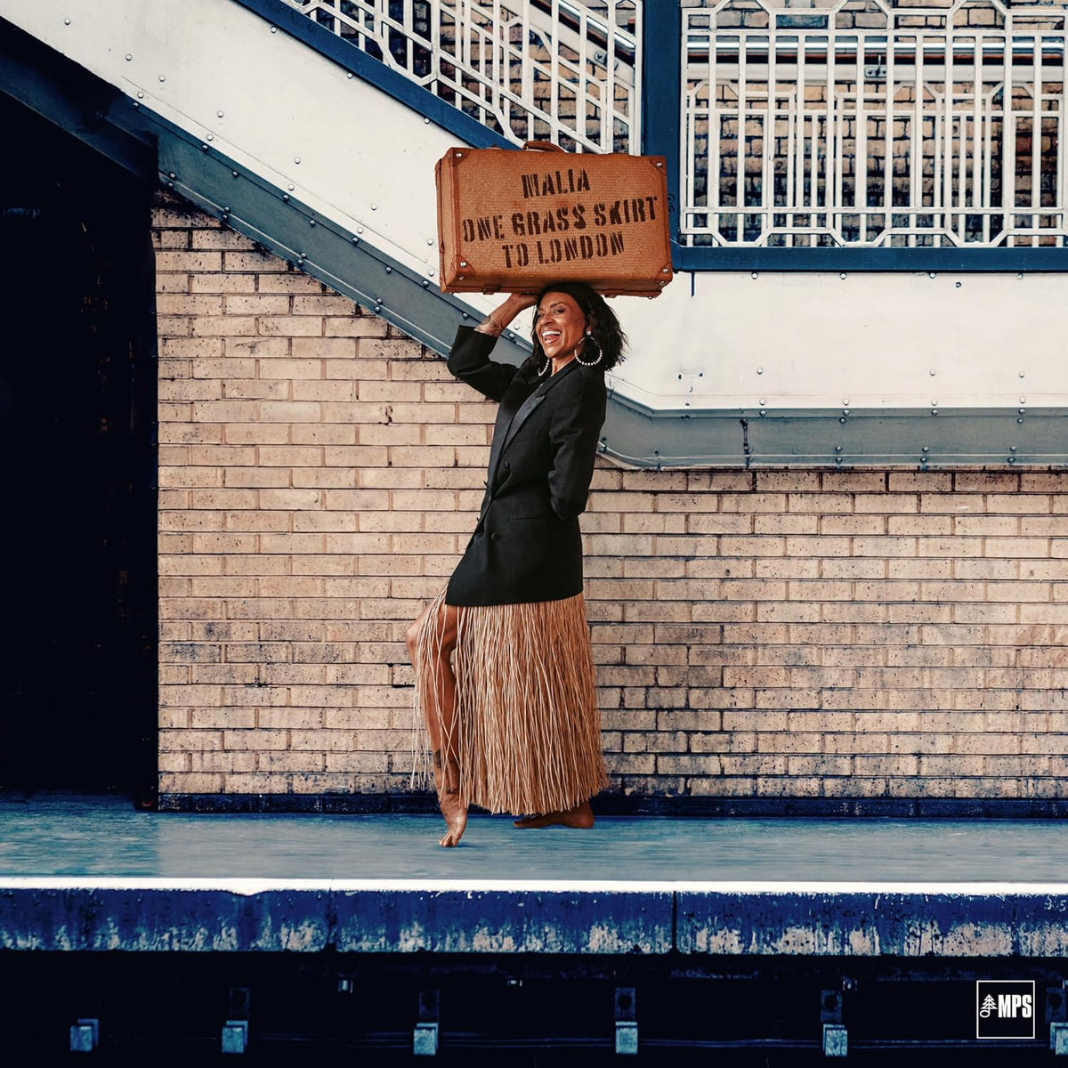 Woman in a grass skirt and blazer poses under a railway arch.