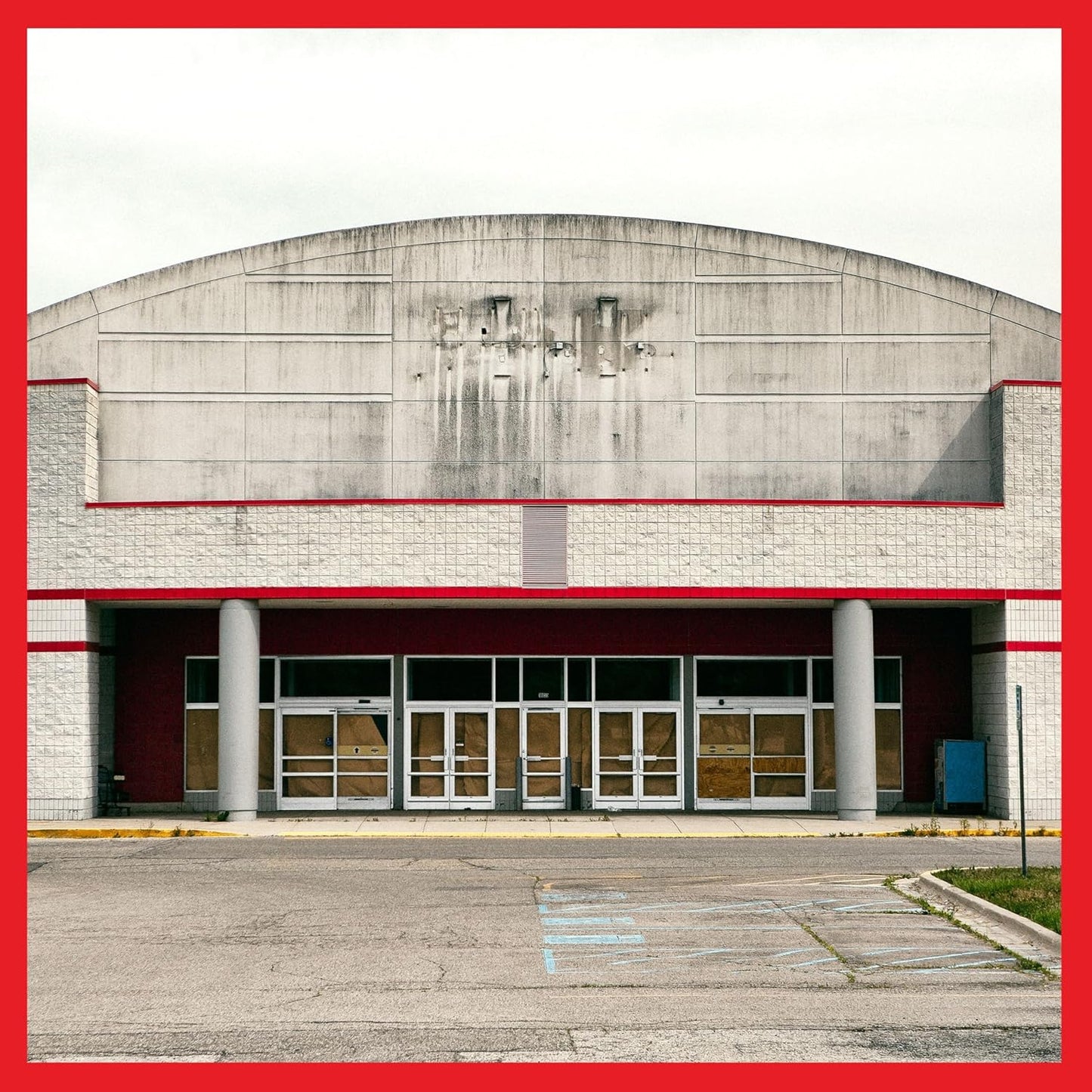 Abandoned concrete building facade with darkened windows and a red border.