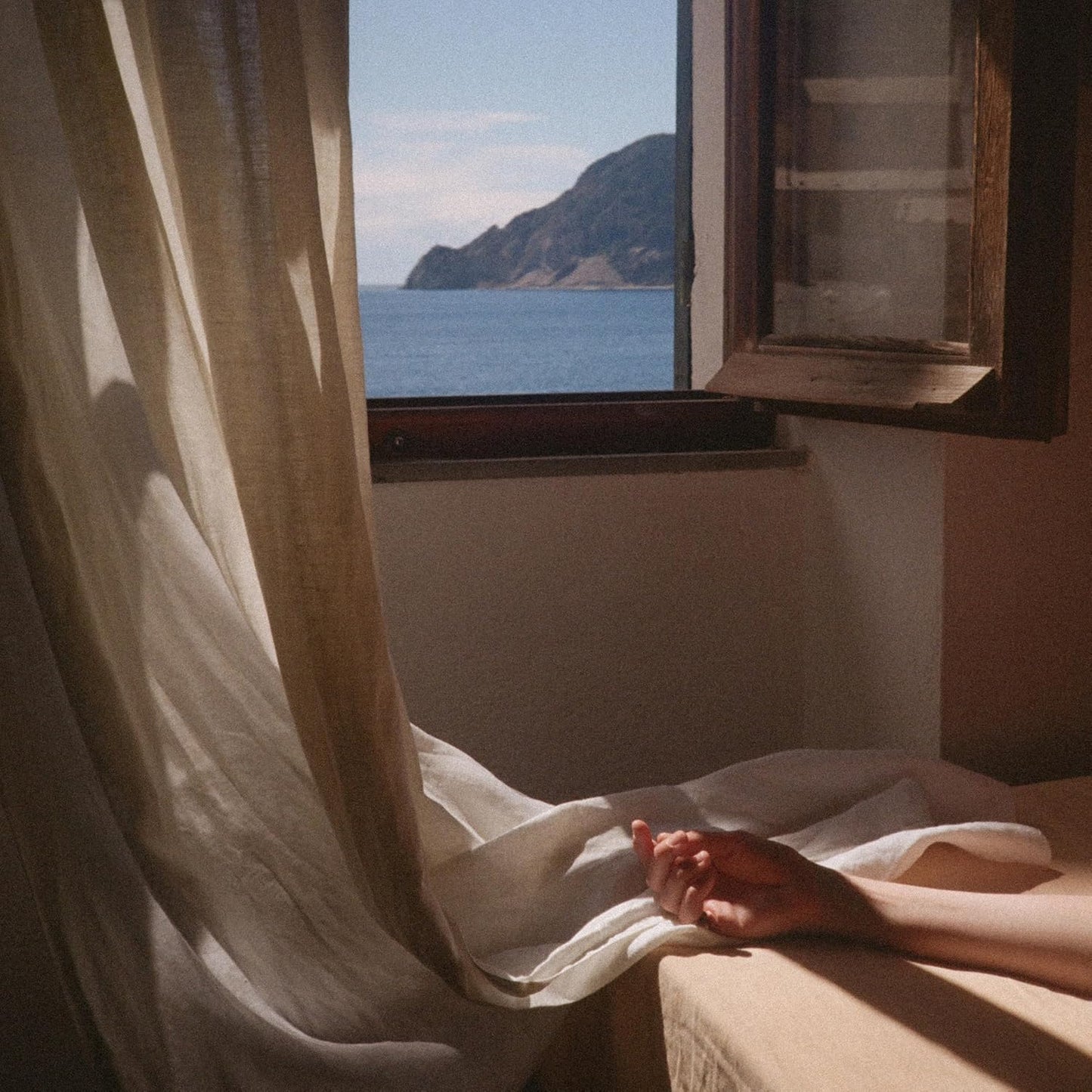 Person resting near a window overlooking the sea, bathed in sunlight.