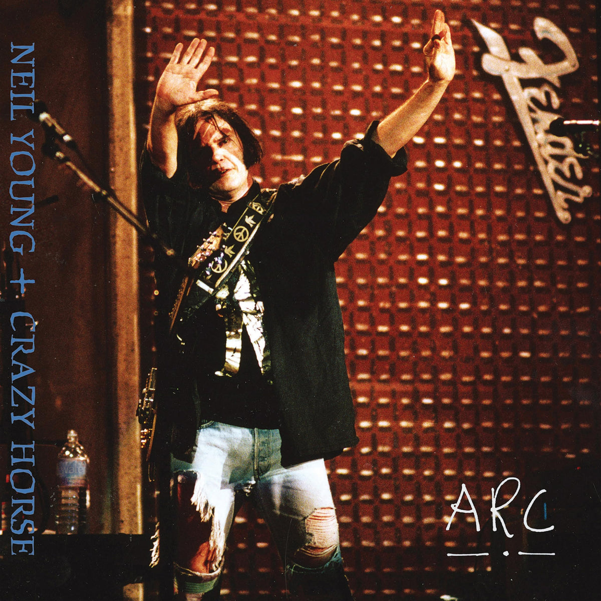 Neil Young performing with arms raised on album cover for "Arc".