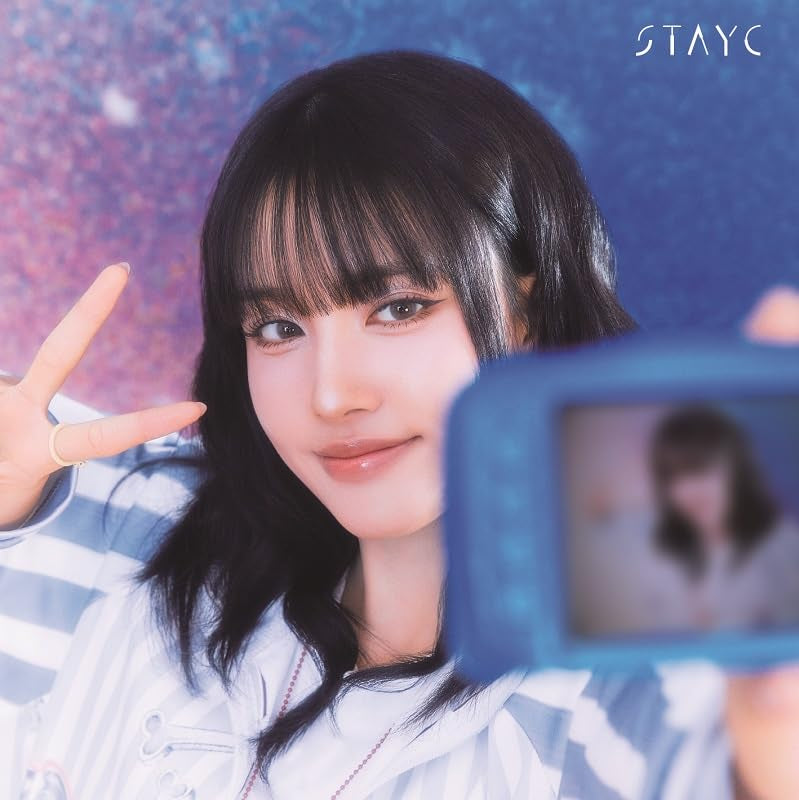 A young woman with dark hair makes a peace sign while holding a blue camera.
