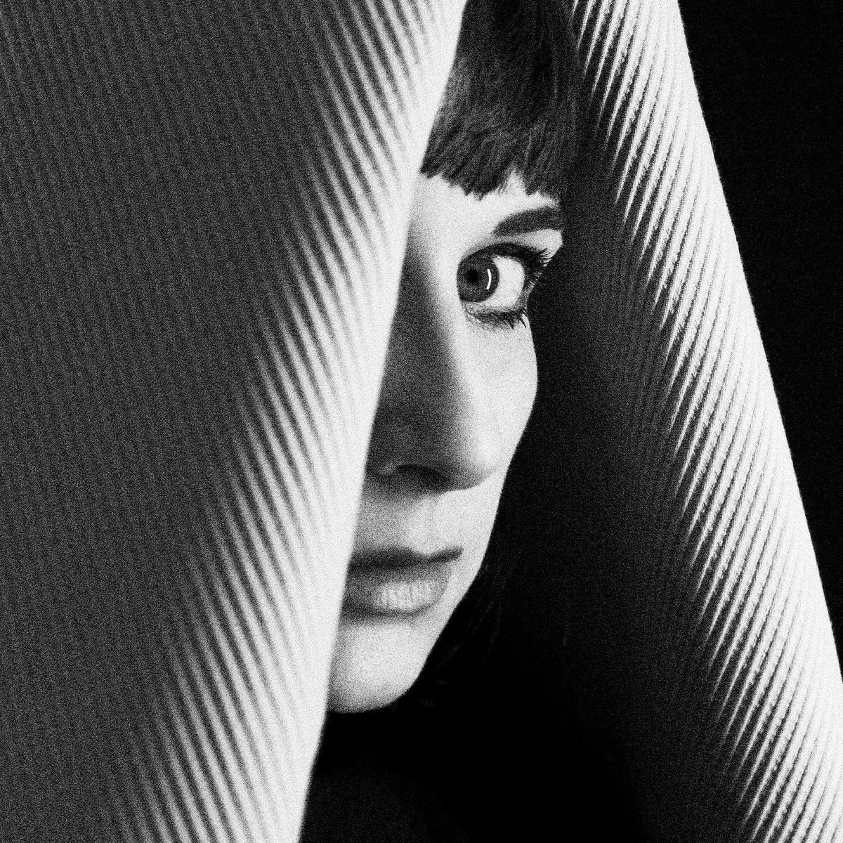 Black and white portrait of a woman partially obscured by striped fabric.