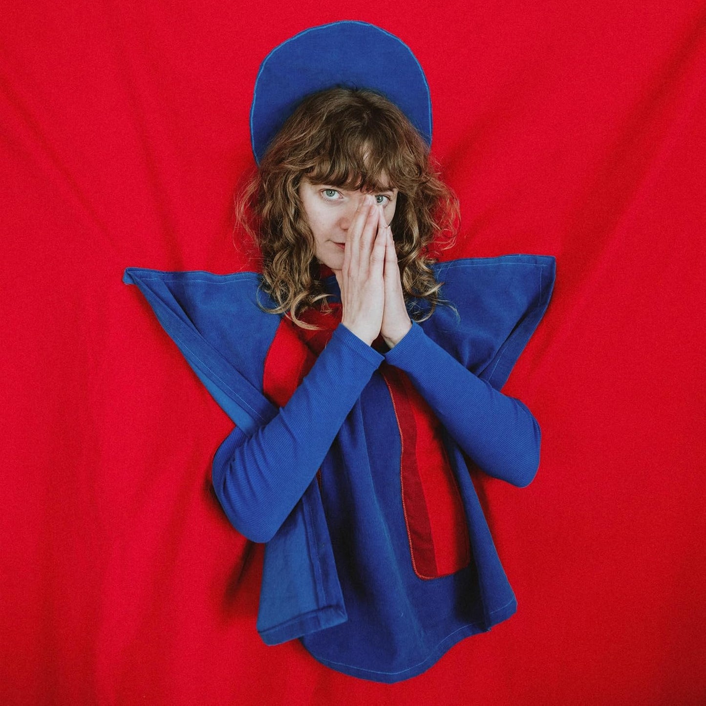 Woman in blue and red clothing, hands covering face, red background.