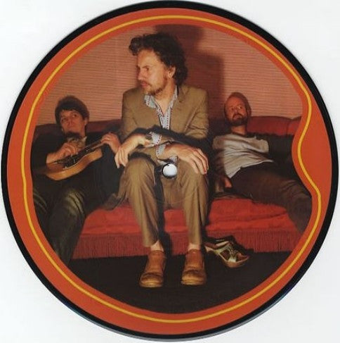 Circular vinyl record featuring three men in suits on a red sofa.
