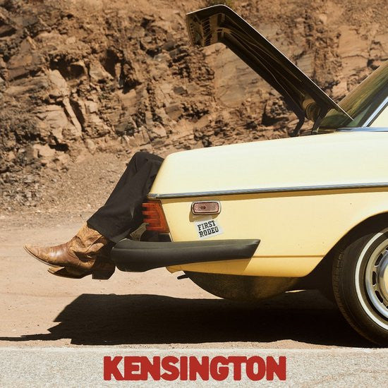 Yellow car with open trunk, legs and cowboy boots visible.