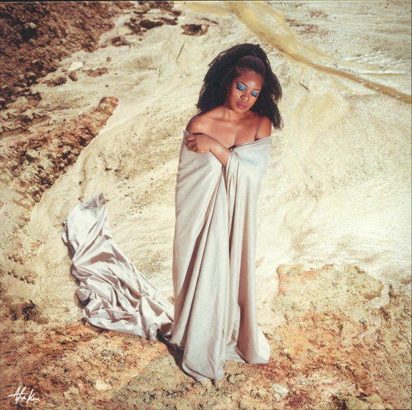Woman in a light-colored wrap stands in a rocky, earthy landscape.