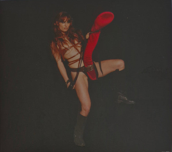 Woman in leather and red stocking mid-kick against a dark background.