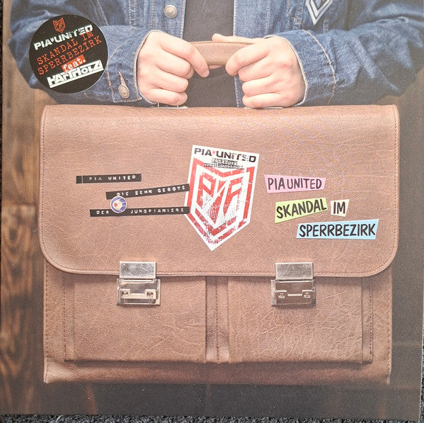 Brown briefcase with stickers and text: "Pia United - Die 10 Gebote".