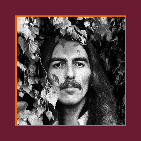 Black and white portrait of a man with long hair, framed by leaves.