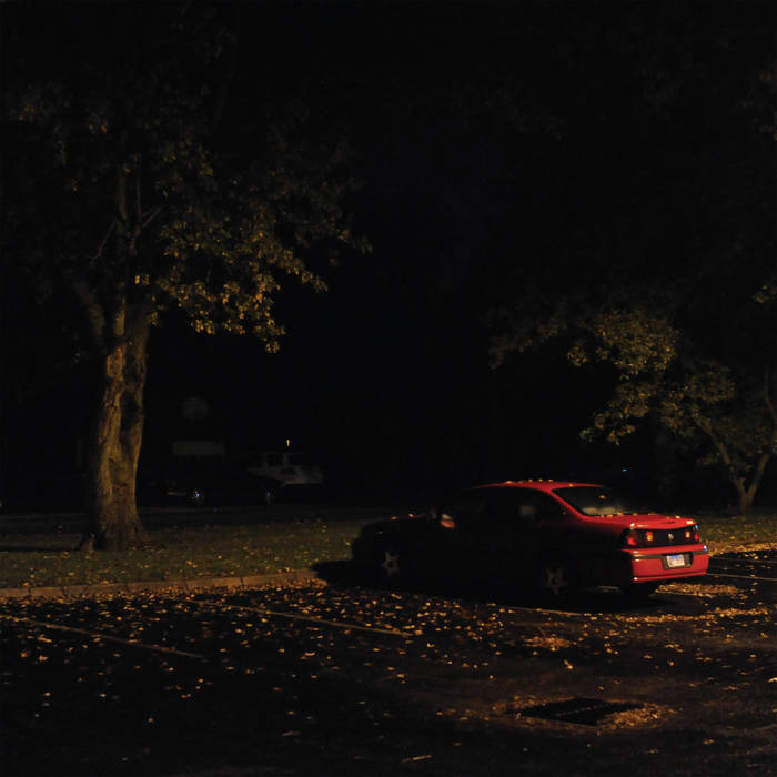 Red car parked under a tree at night, dark and moody.