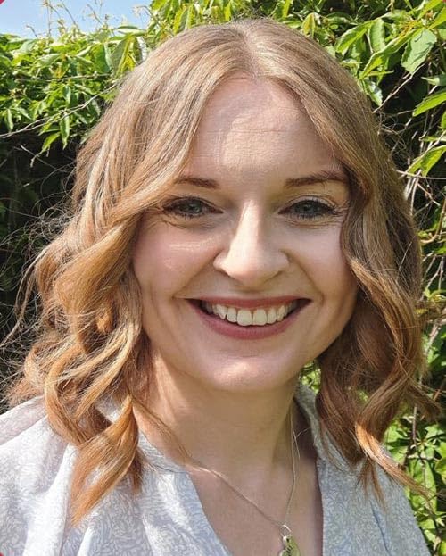 Close-up portrait of a smiling woman with wavy, light brown hair.