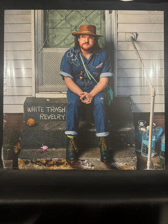 Man in denim overalls and hat sits on porch steps.