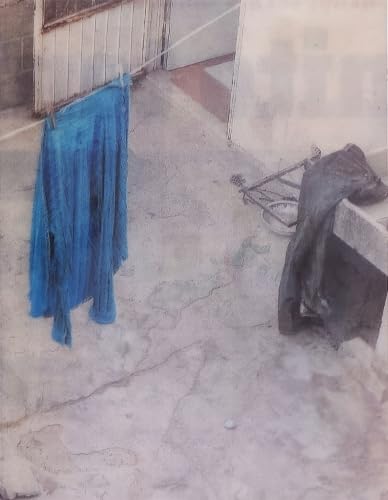 Blue clothing hangs on a line above cracked concrete and objects.