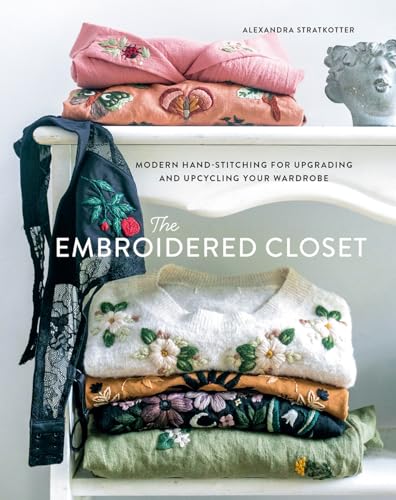 Book cover with embroidered clothing stacked on a white shelf.