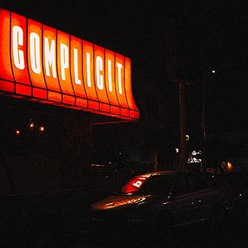 Red neon sign spelling "COMPLICIT" above a dark, blurry street scene.