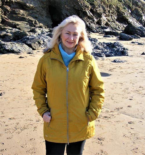 Woman with blonde hair wearing a yellow jacket on a beach.