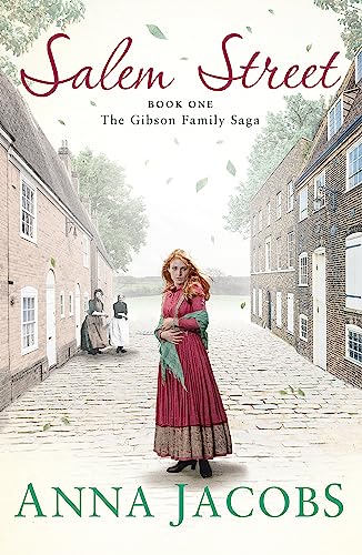 A woman in a long red dress stands on a cobblestone street between buildings.