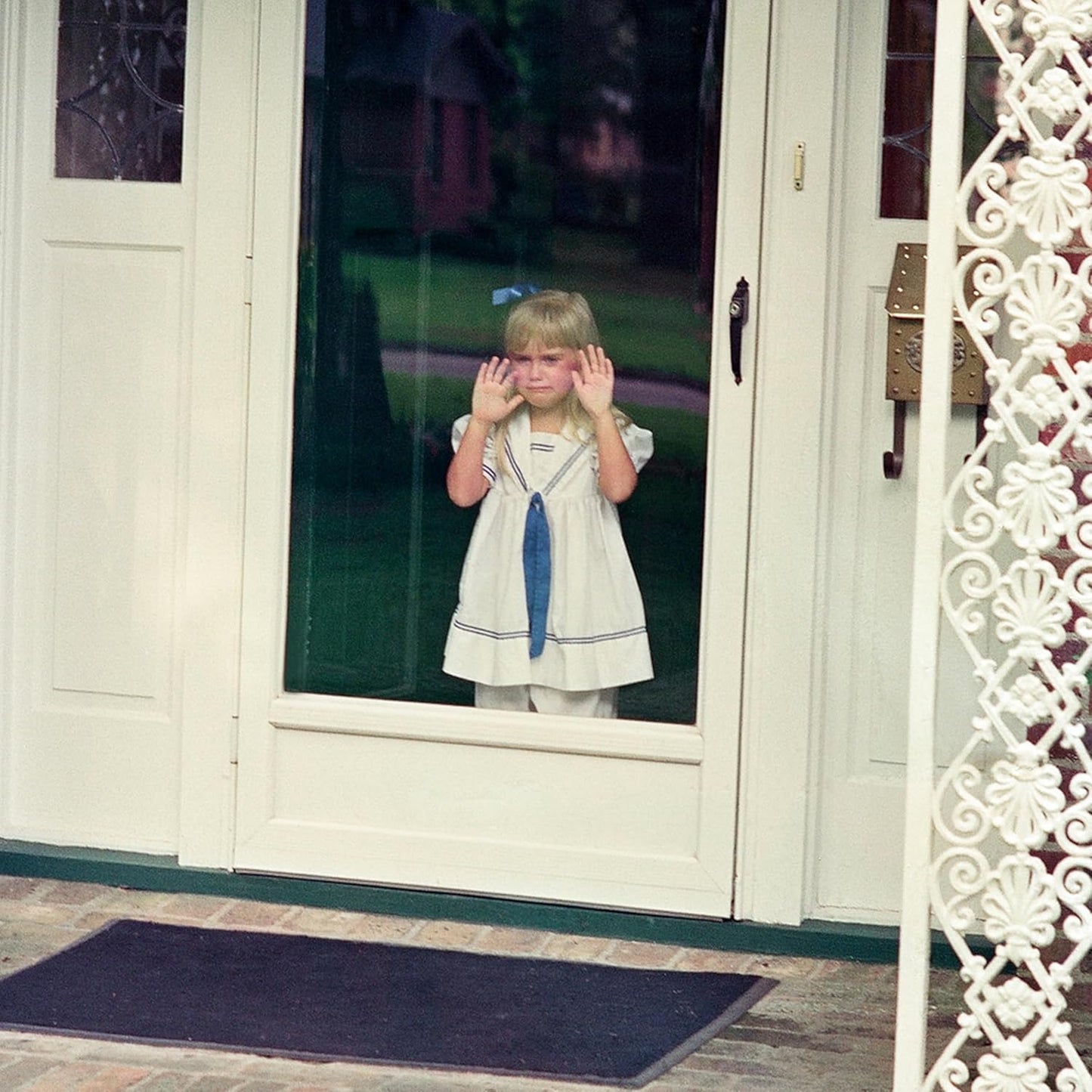 Young girl framed in a doorway, hands covering her ears.