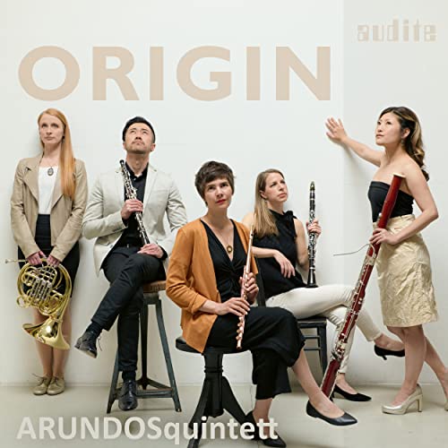 Five musicians with wind instruments pose against a white background.