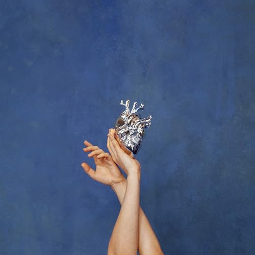 Silver anatomical heart held in hands against a blue backdrop.