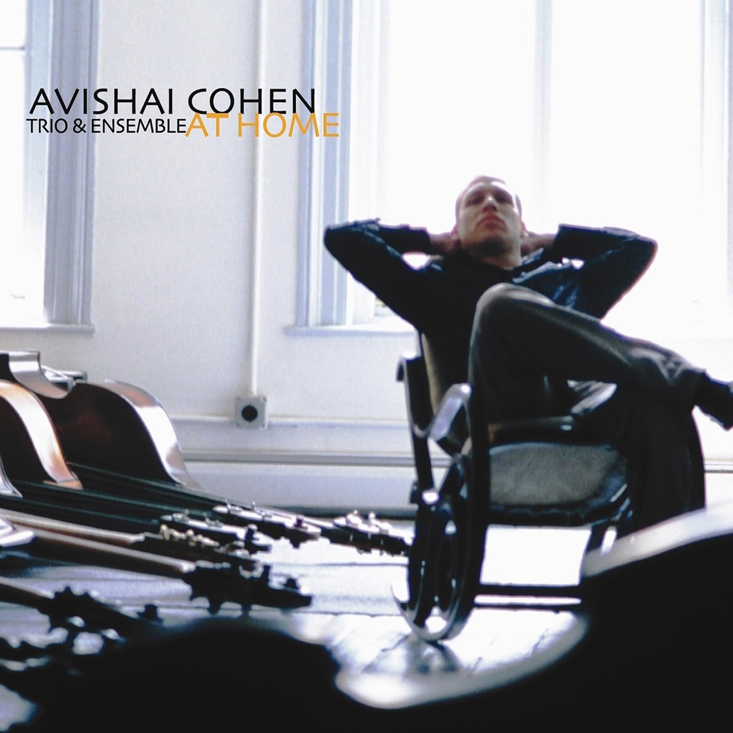 Avishai Cohen sits in a chair with double basses resting on the floor nearby.