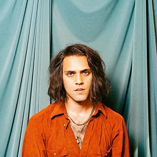 Portrait of a man with long hair wearing an orange shirt.
