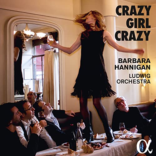 Woman in black dress dancing on a dining table with onlookers.