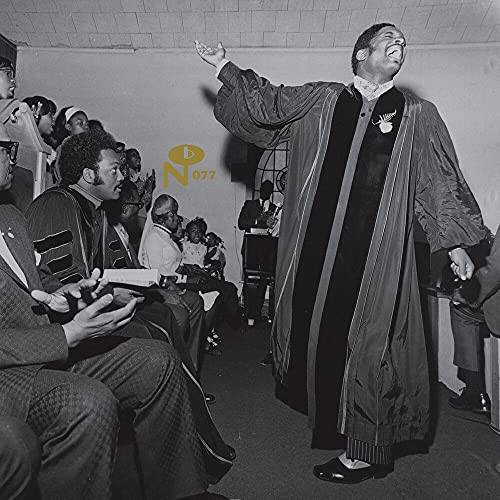 Black and white photo of a pastor with raised hands, preaching to a congregation.