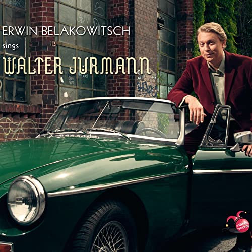 Man in red jacket poses by a green vintage convertible car.