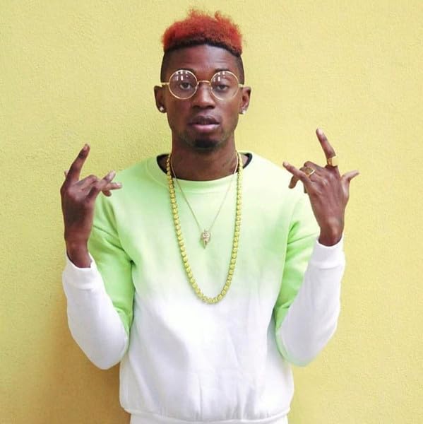Young Black man with dyed hair and glasses, making hand gestures.