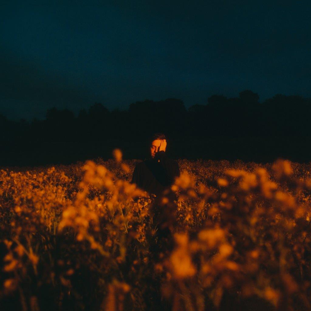 Man standing in a field of orange flowers, dark background.