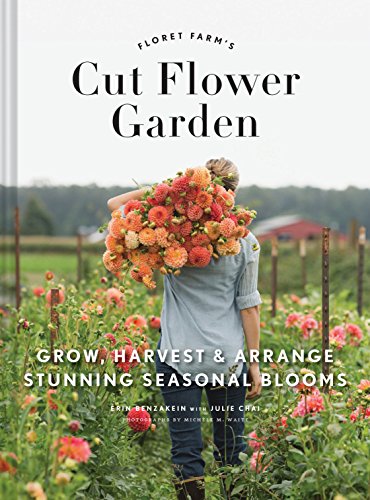 A person carries a large armful of orange dahlias through a flower field.