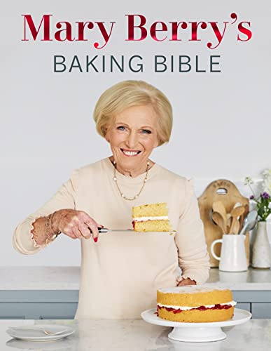 Mary Berry holding a slice of cake on a spatula in front of a cake.