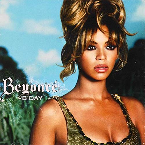 Beyoncé with an updo hairstyle wearing a gold top against a blue sky background.