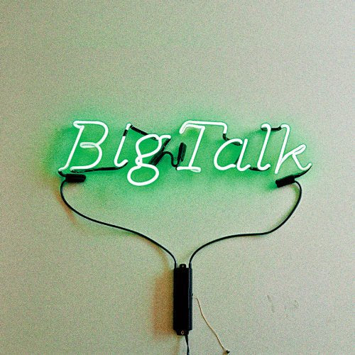 Green neon sign spelling “Big Talk” against a pale wall.