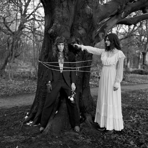 Black and white photo of two people in a forest, one gesturing towards the other.