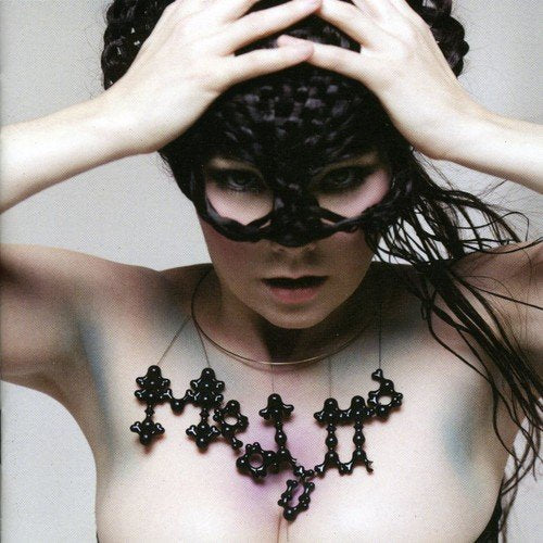 Björk in a black, textured mask and beaded necklace, close-up portrait.
