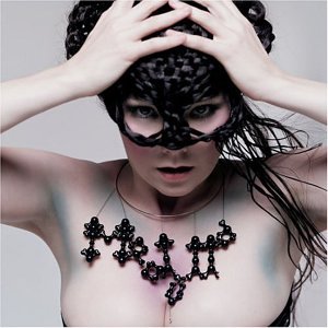 Björk in a black lace mask and beaded necklace, looking at the viewer.