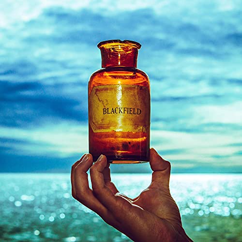 A hand holds an amber glass bottle labeled Blackfield against a blue ocean background.