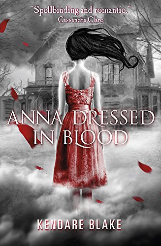 A girl with long dark hair in a blood-stained dress stands before a house.