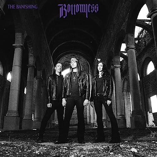 Three band members in black leather jackets standing inside a ruined stone building.