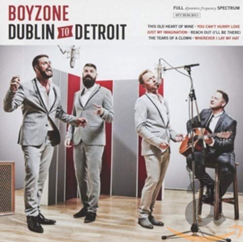 Four men in suits singing and playing guitar in a recording studio setting.