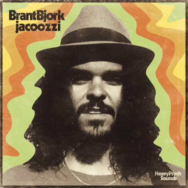 Album cover featuring a man with long hair and a hat against wavy colors.