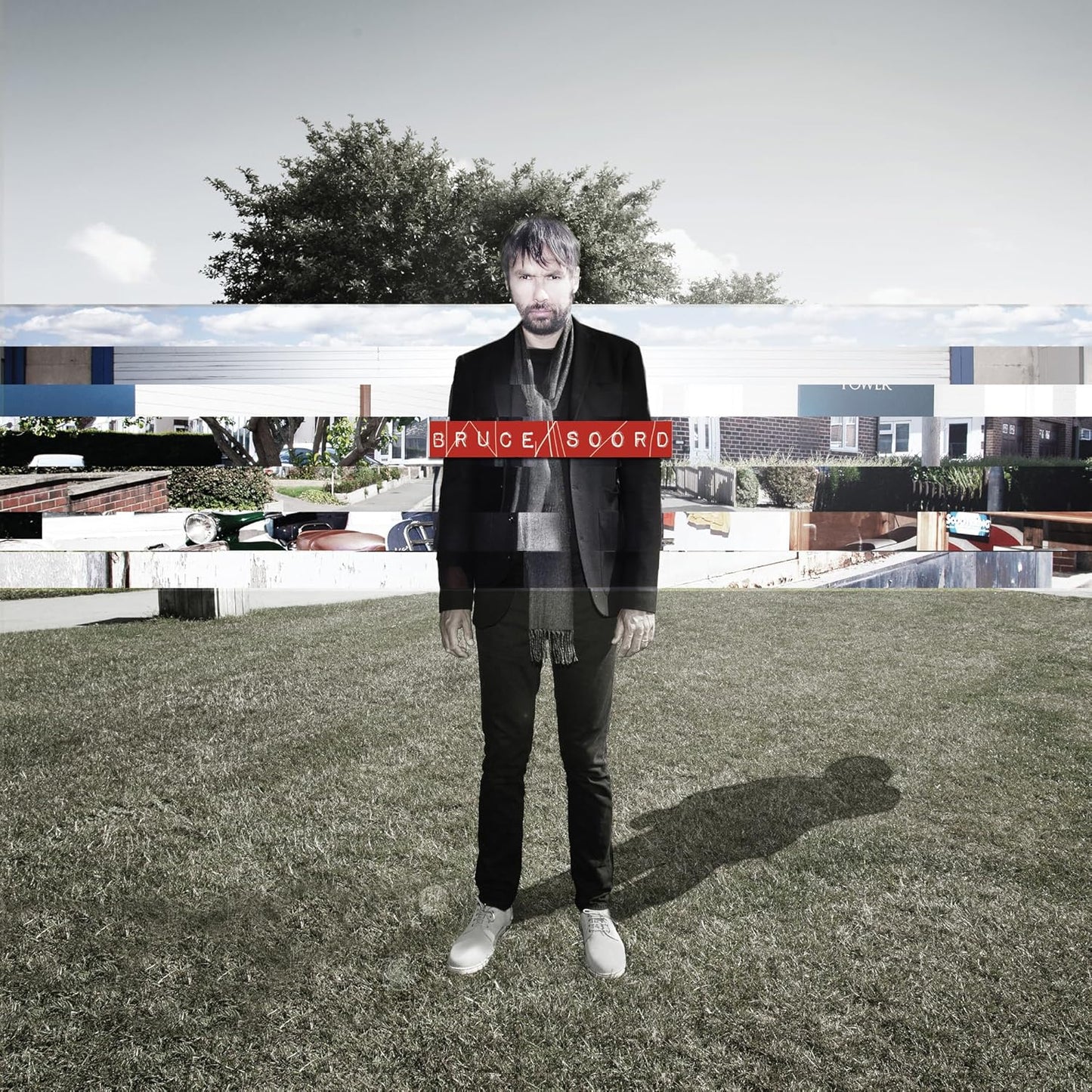 Man in black suit standing on grass with building backdrop.