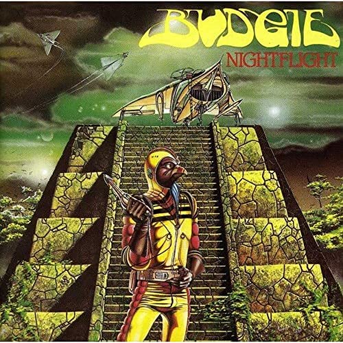 A bird-headed figure in a yellow suit stands before a stone pyramid at night.