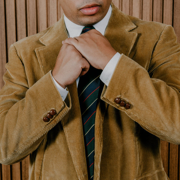 Man in brown corduroy suit and tie, hands clasped at chest.