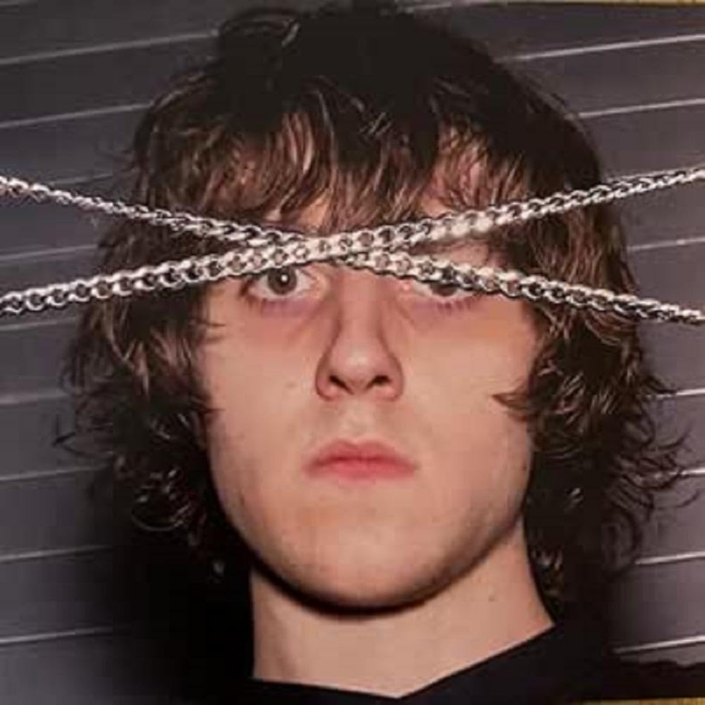 Close-up of a young man with curly hair and a chain across his eyes.