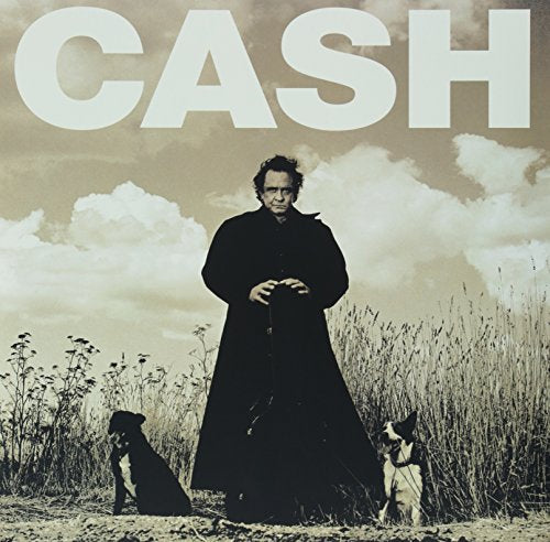 Johnny Cash in a black coat stands with two dogs in a field.