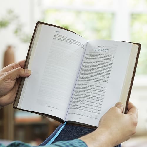 Open black leather Bible with text and devotions, held in hands.