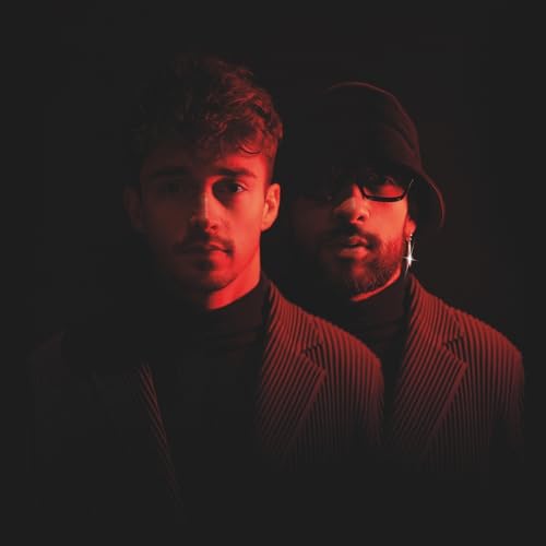 Two young men with dark hair, lit with red tones, pose closely.